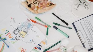 A colorful child's drawing of a family alongside pizza and pens on a table.